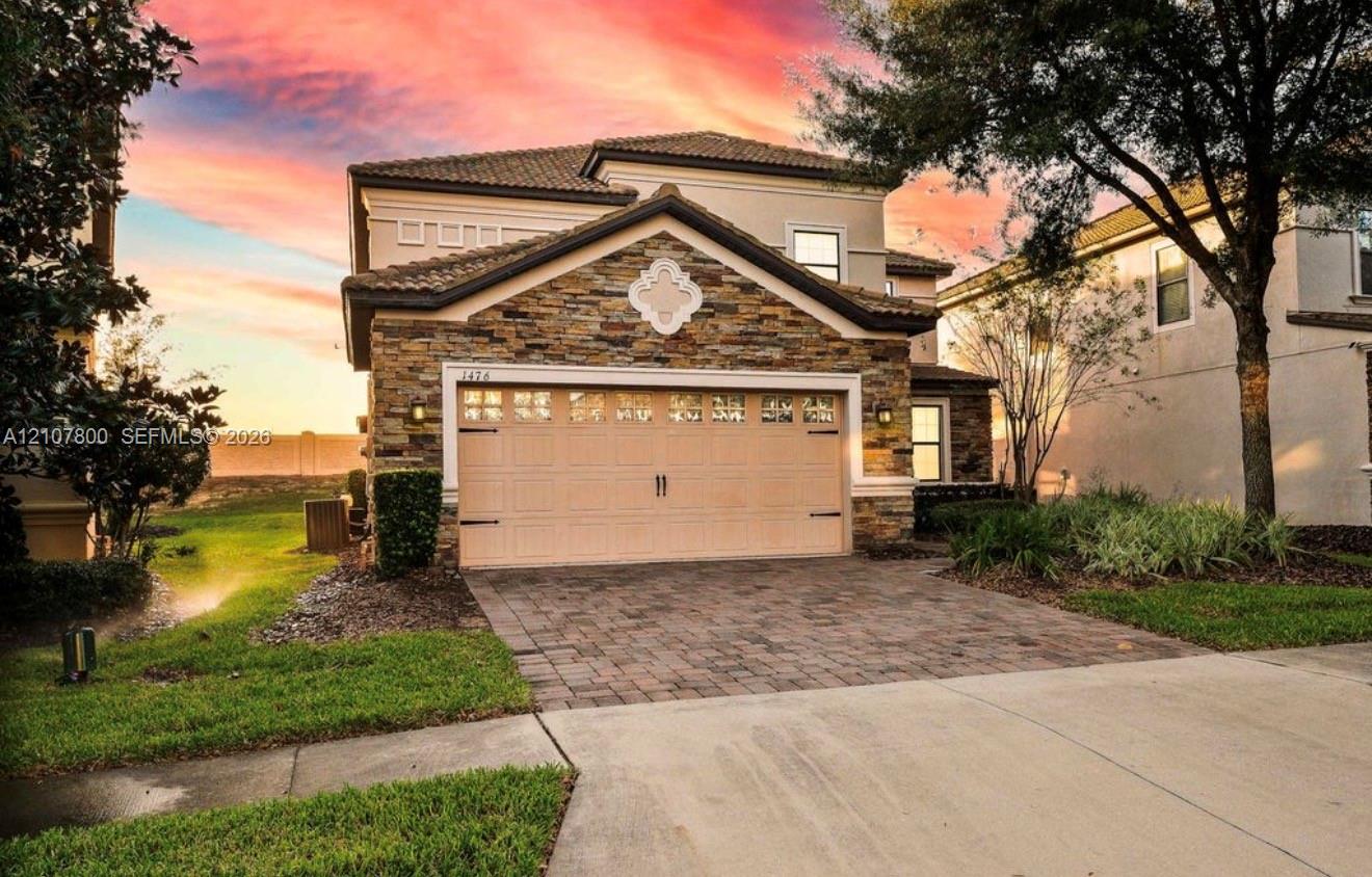 Two-story residence featuring stacked stone veneer, a multi-paneled garage door, decorative gable medallion, tile roofing, and a paved stone driveway