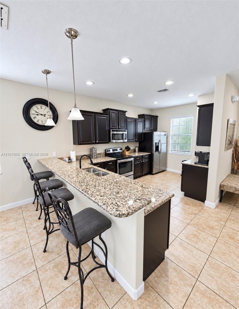Kitchen featuring dark cabinetry, expansive stone-finish countertops, stainless steel appliances, dual pendant lighting, and ceramic tile flooring