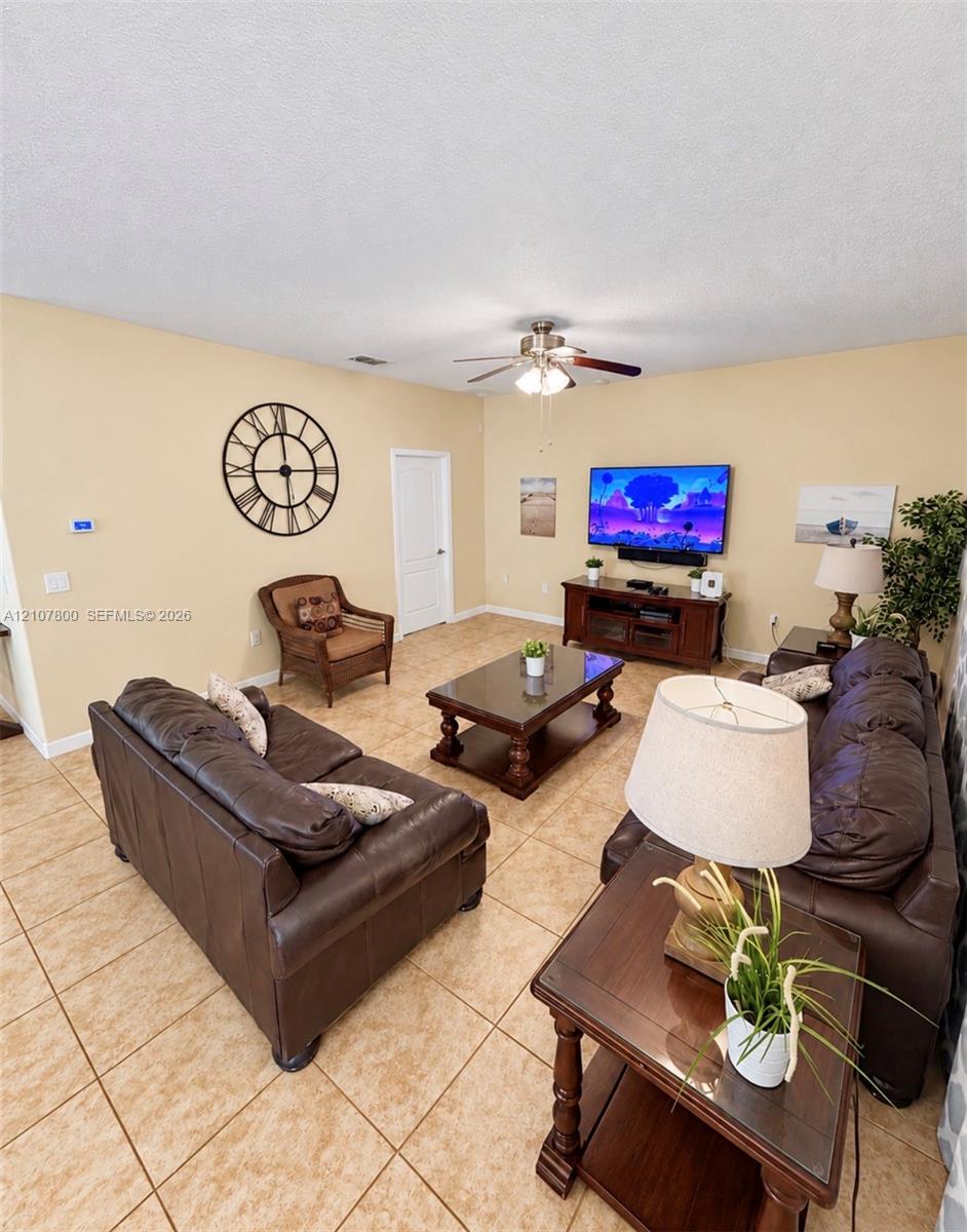 Neutral-toned living space featuring large-format ceramic tile flooring, a central ceiling fan with integrated lighting, and a solid-core interior door