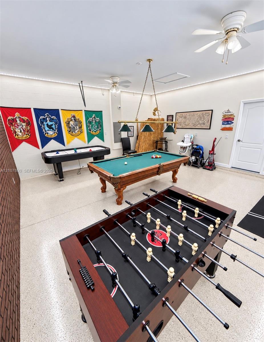 Expansive multi-use room featuring an exposed brick wall, speckled epoxy flooring, recessed LED perimeter lighting, and dual ceiling fans