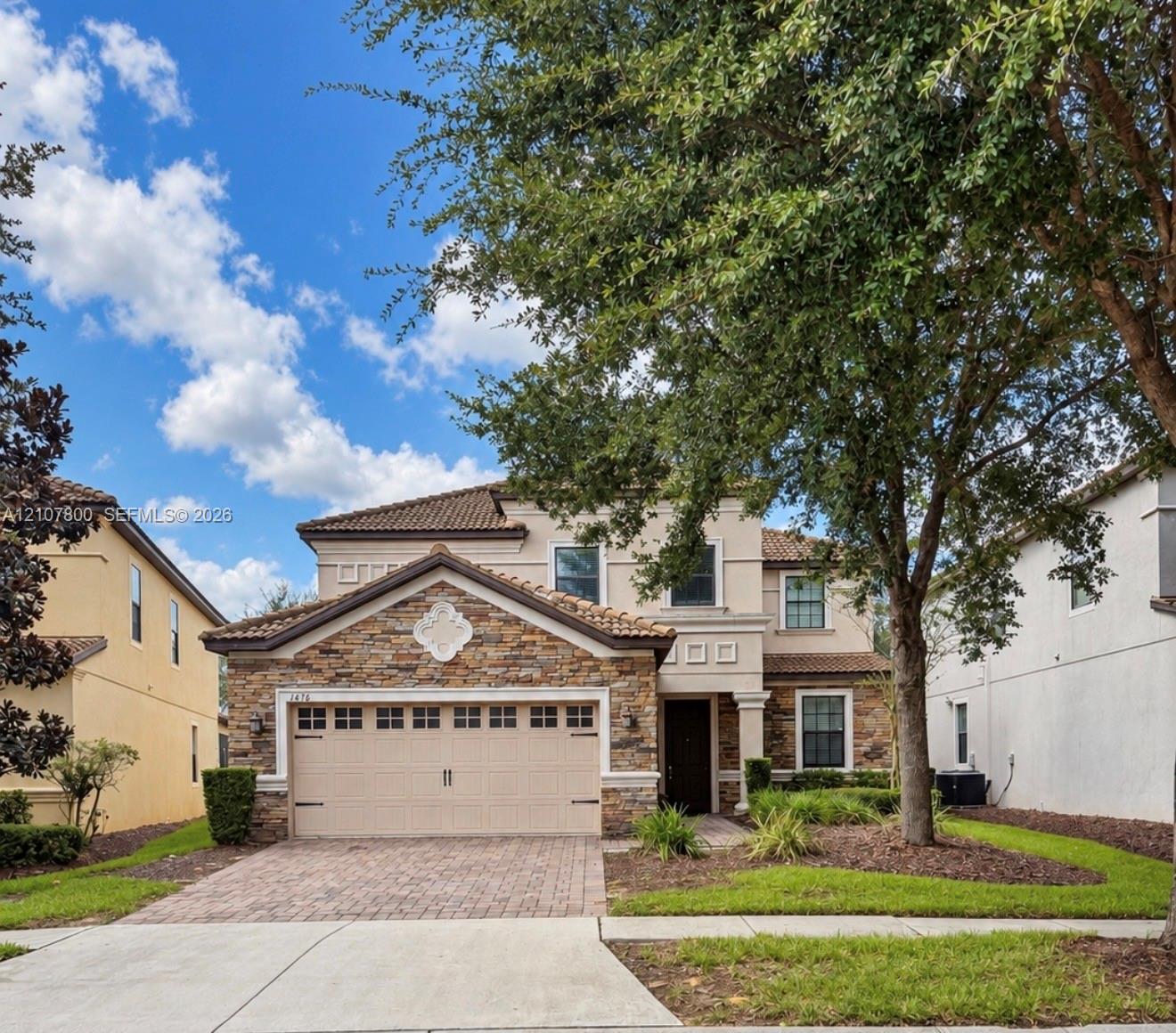 Two-story exterior featuring a stone veneer facade, tile roofing, an attached multi-car garage, and a brick-paver driveway Two-story exterior featuring a stone veneer facade, tile roofing, an attached multi-car garage, and a brick-paver driveway