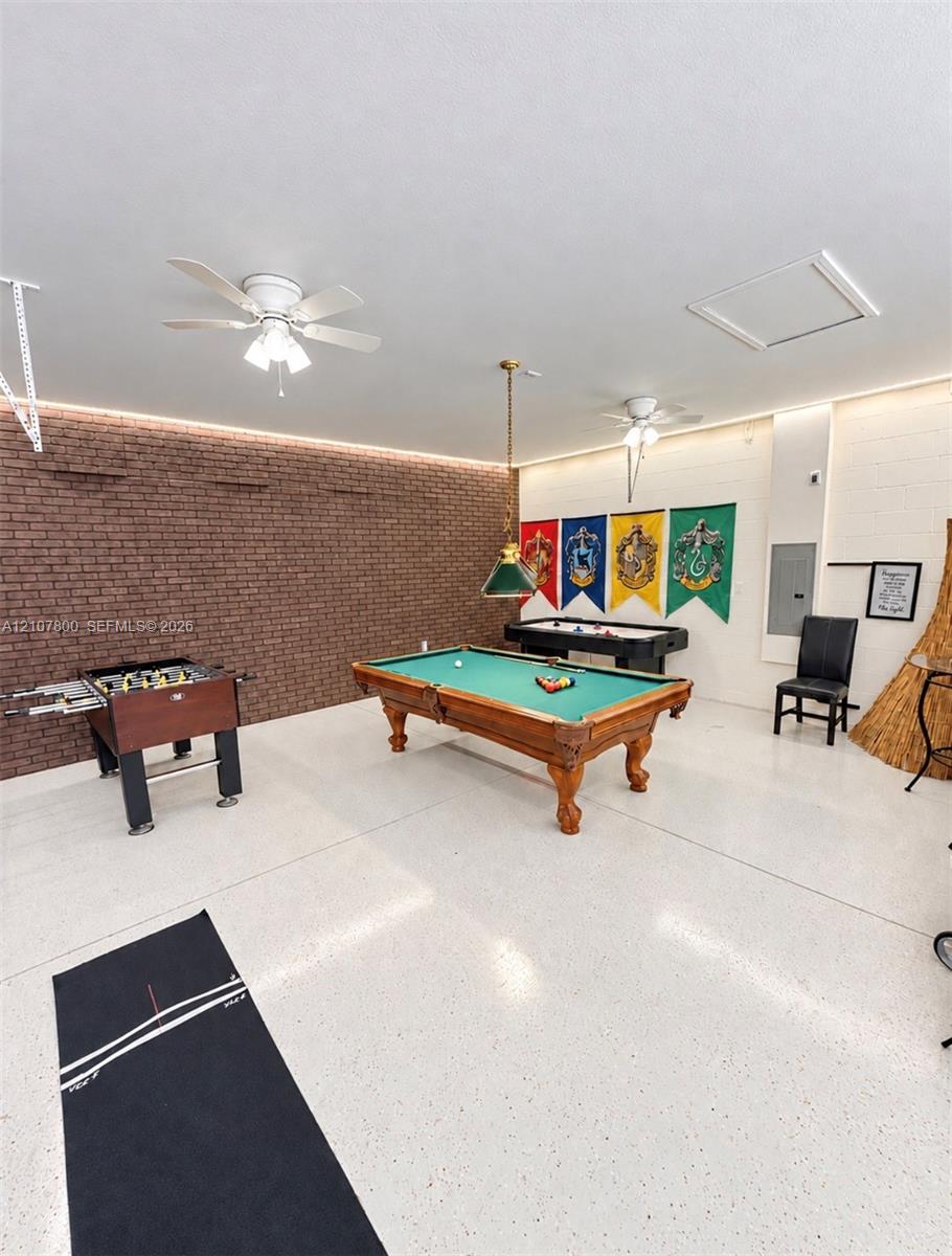 Interior space featuring a brick accent wall, white speckled epoxy flooring, two ceiling fans, recessed perimeter lighting, and a pendant light fixture