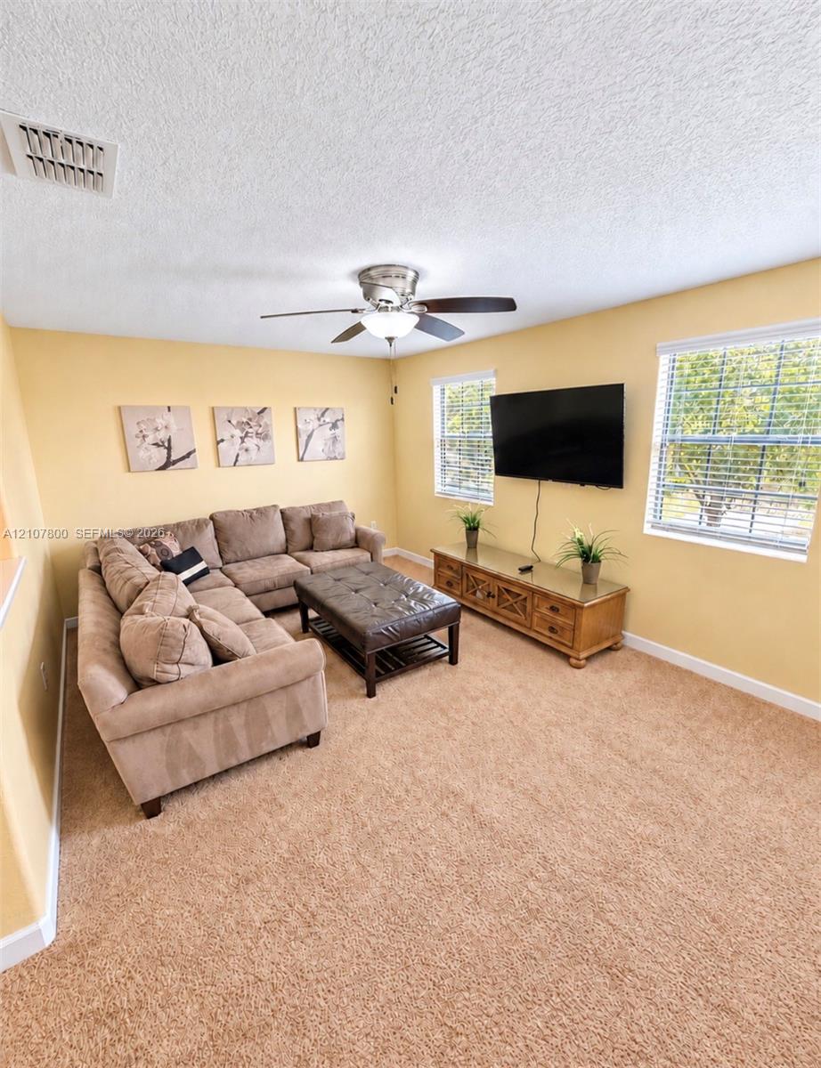 Living area featuring wall-to-wall carpeting, dual windows, and a ceiling fan with light fixture