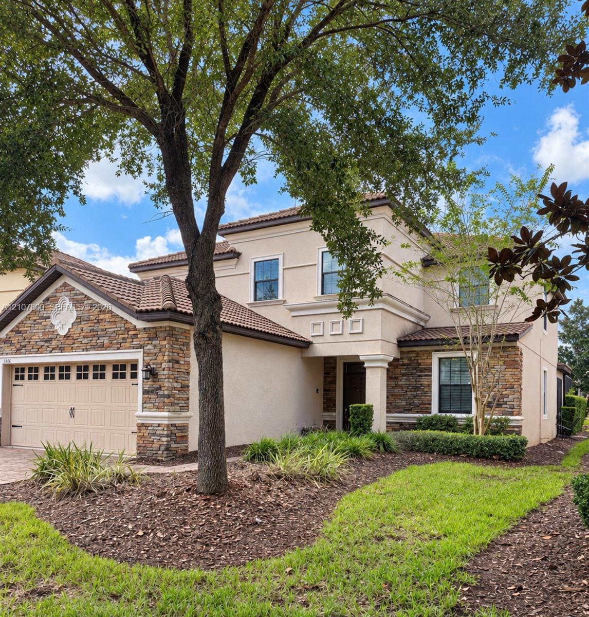 Two-story stucco exterior featuring stone masonry accents, a tiled roof, multi-pane windows, and a multi-car garage