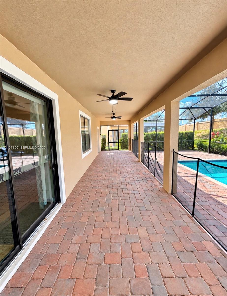 Covered patio featuring brick-paver flooring, dual ceiling fans, sliding glass door access, and a screened-in pool enclosure