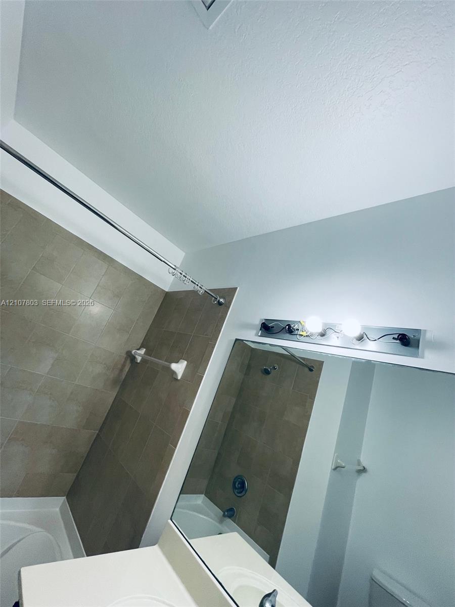 Bathroom featuring neutral wall tiling, a built-in tub, a large vanity mirror, and multi-bulb wall-mounted lighting