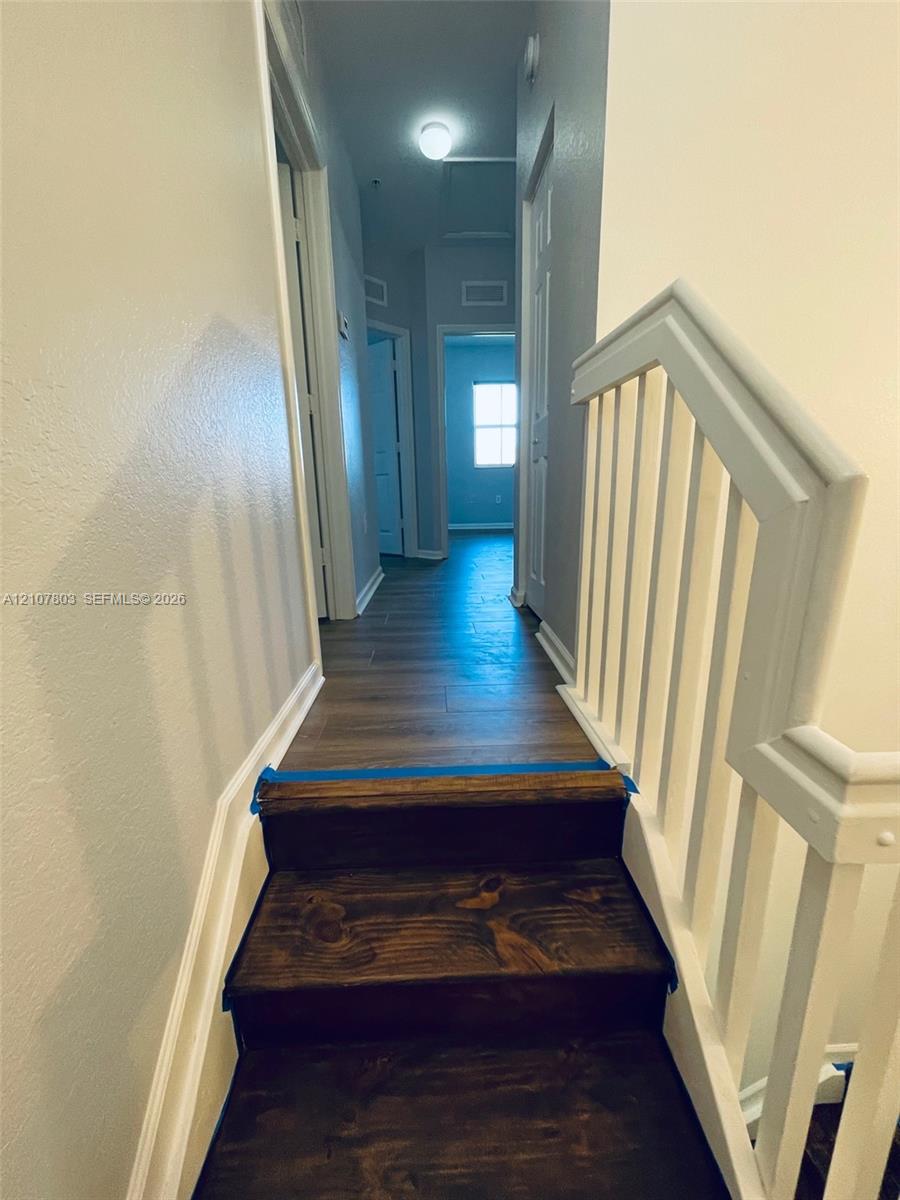 Staircase with wood-finish treads and white balustrade, featuring wood-finish flooring and multiple interior doors