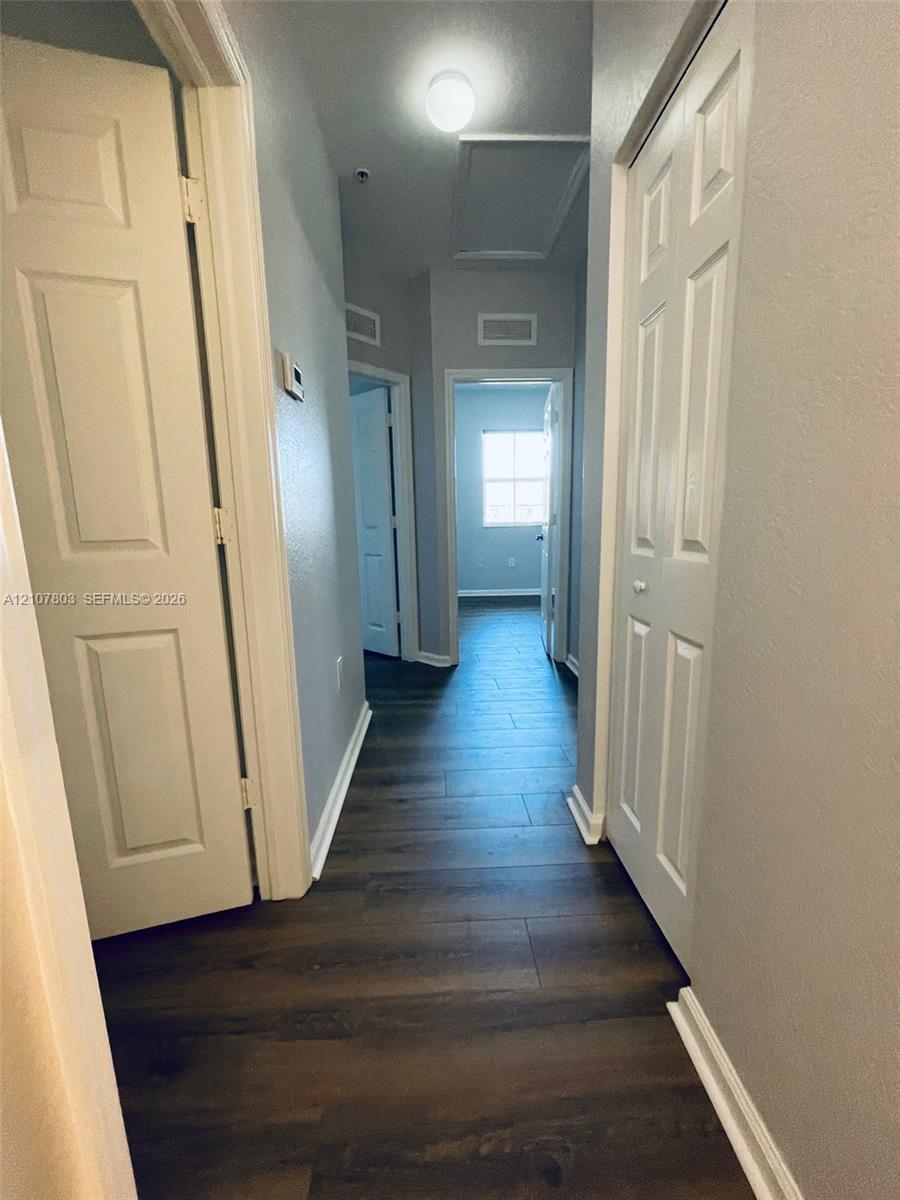 Interior hallway featuring dark-tone wood-finish flooring, paneled interior doors, and overhead flush-mount lighting