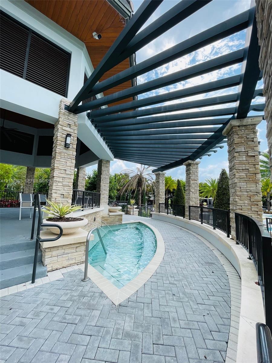 Custom outdoor space featuring a stone-columned pergola, curved pool with integrated entry stairs, paved herringbone patio, and wood-paneled ceiling details