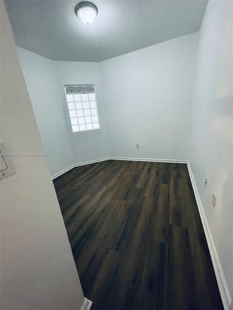 Multi-faceted room featuring wood-finish flooring, a glass block window, and a central ceiling-mounted light fixture