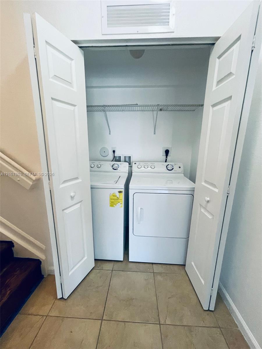 Laundry closet featuring double bi-fold doors, white top-loading washer and dryer, and a wire shelving unit