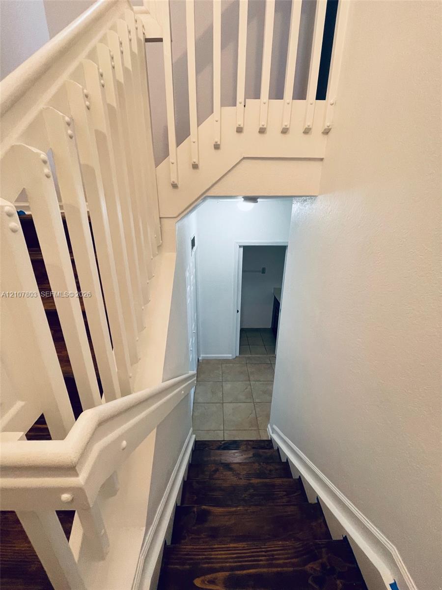 Staircase featuring stained wood treads, white-painted wood balusters, and a solid wood handrail with ceramic tile flooring at the base