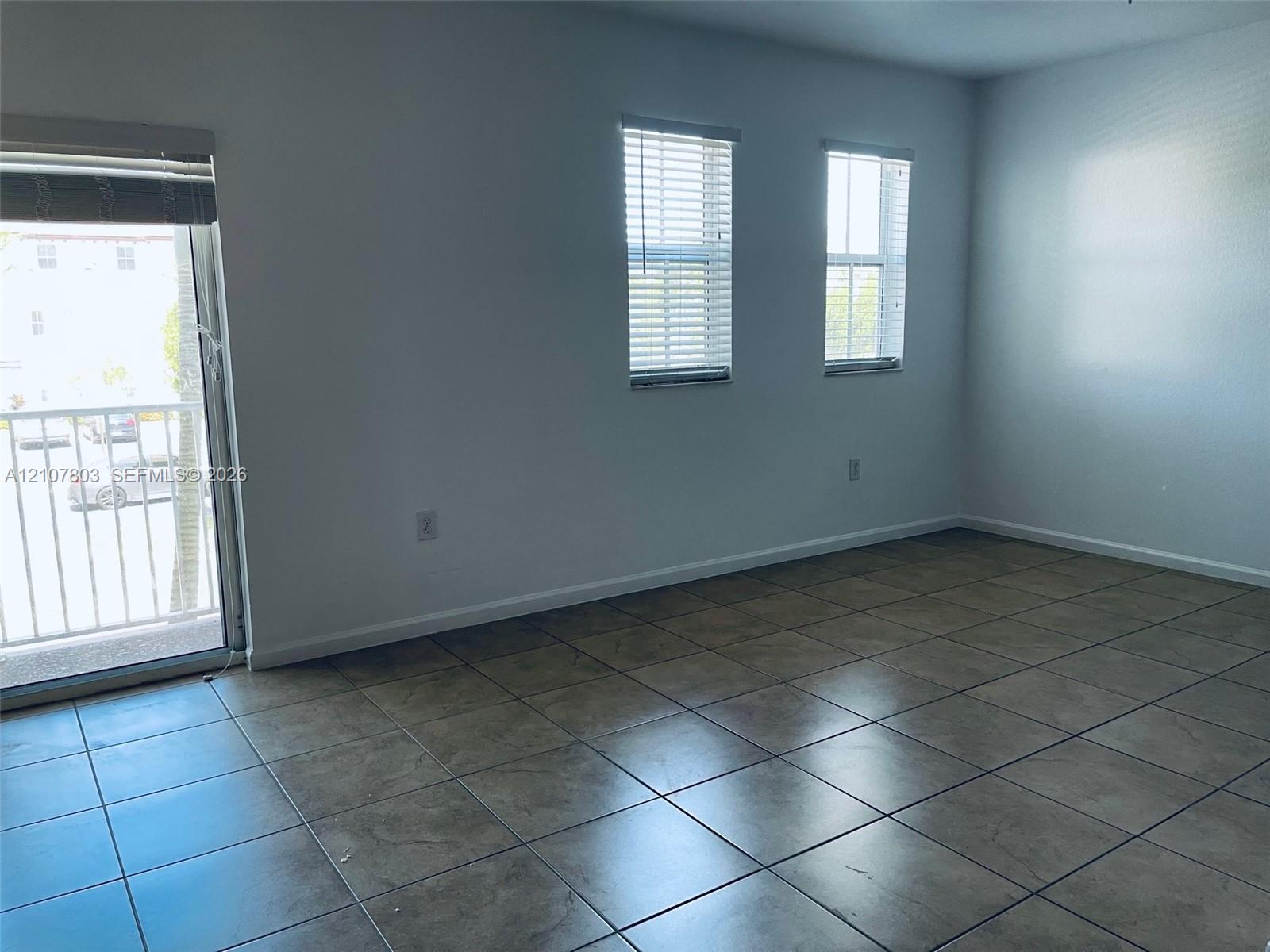 Interior space featuring ceramic tile flooring, two double-hung windows with horizontal blinds, and a sliding glass door with access to an exterior balcony