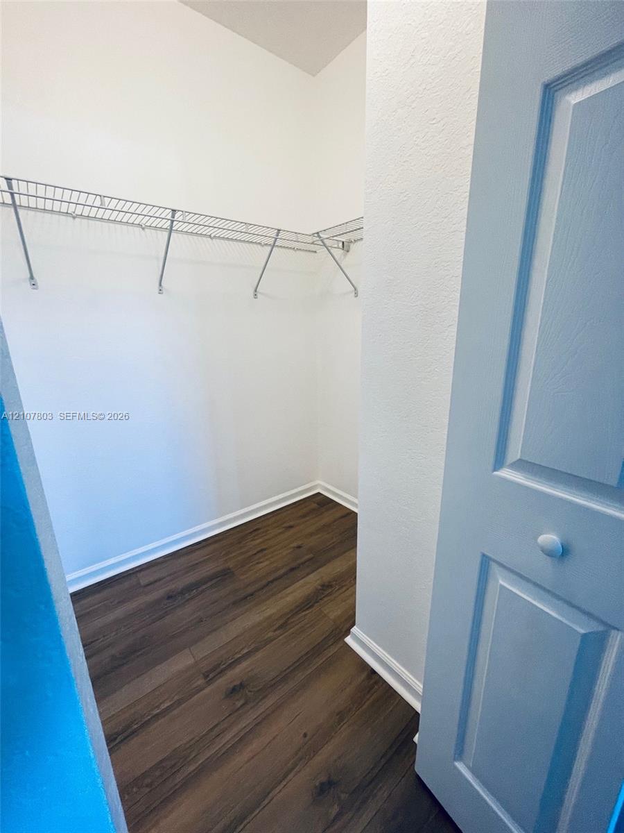 Walk-in storage space featuring wood-finish flooring, white walls, and built-in wire shelving