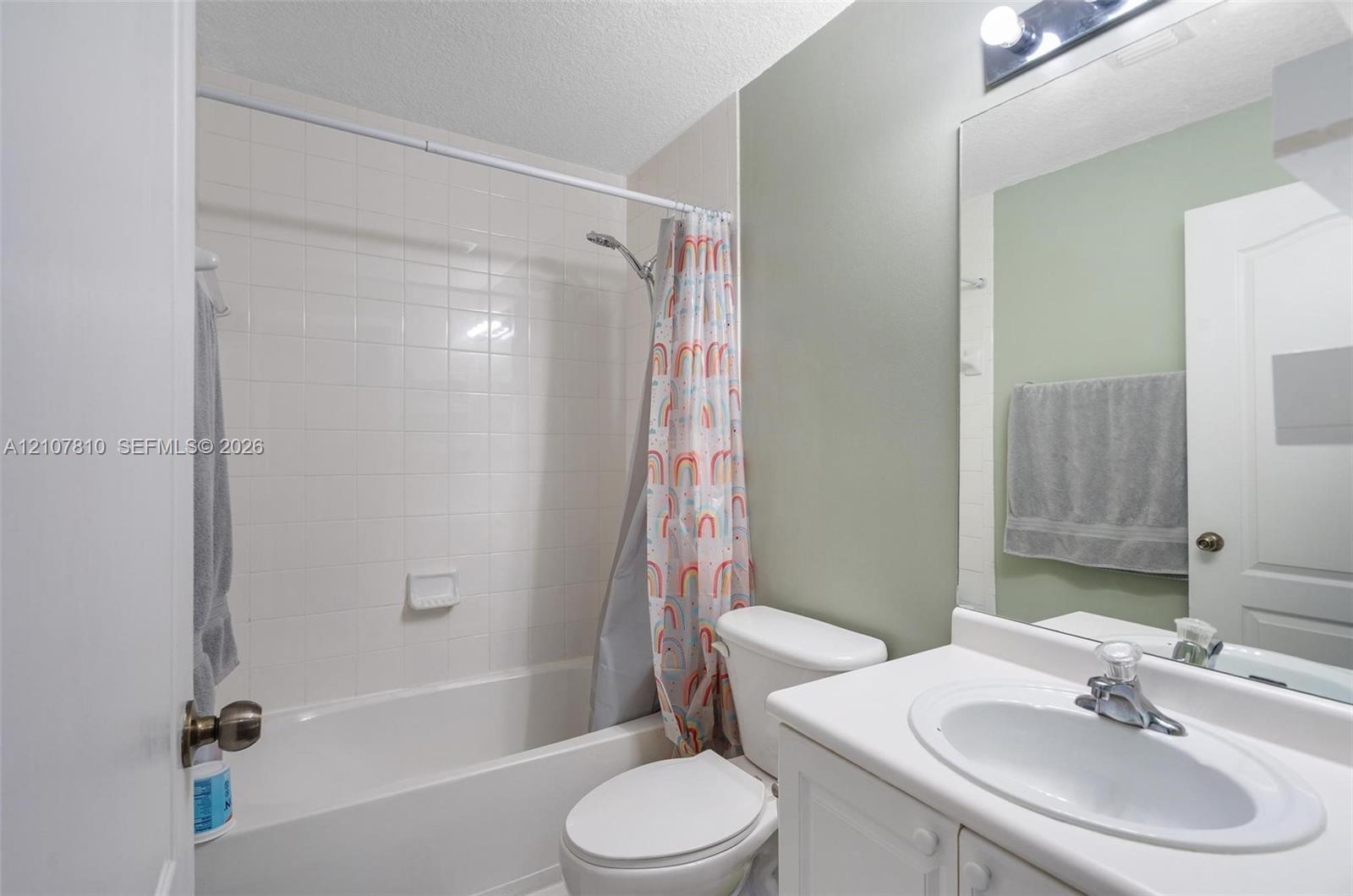 Bathroom featuring a white vanity with an integrated sink, a full-width vanity mirror, a bathtub with a tiled surround, and a wall-mounted light fixture