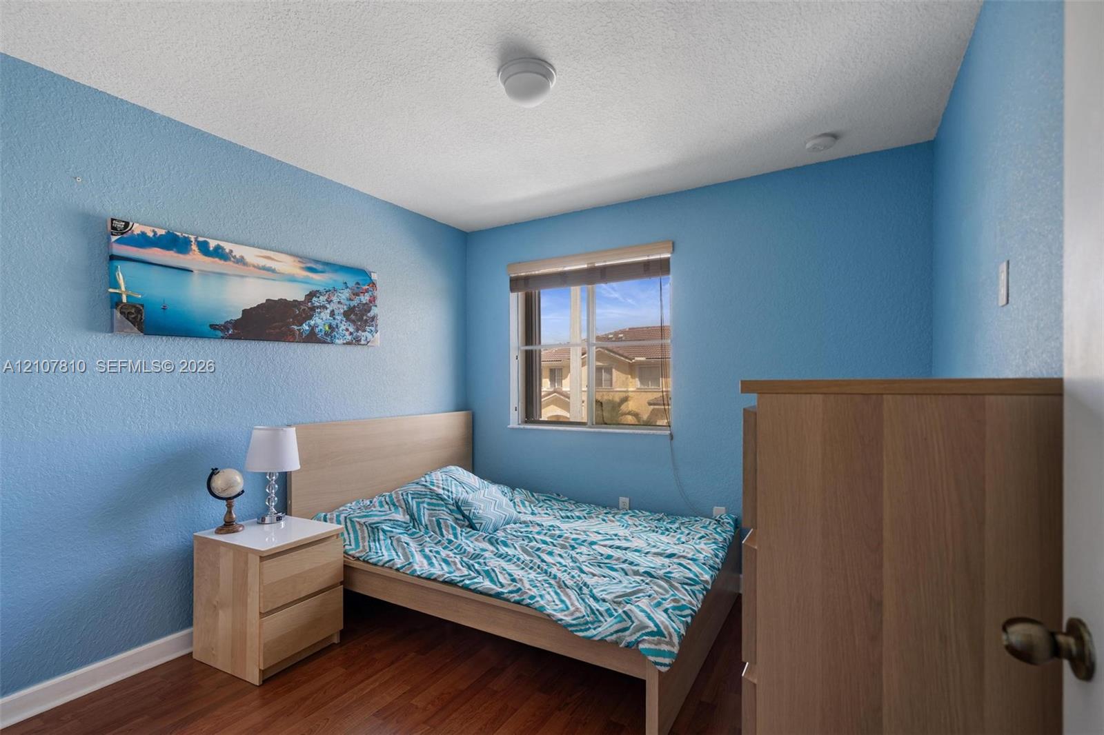 Room featuring wood-finish flooring, textured walls, and a single-pane window with an integrated roller shade