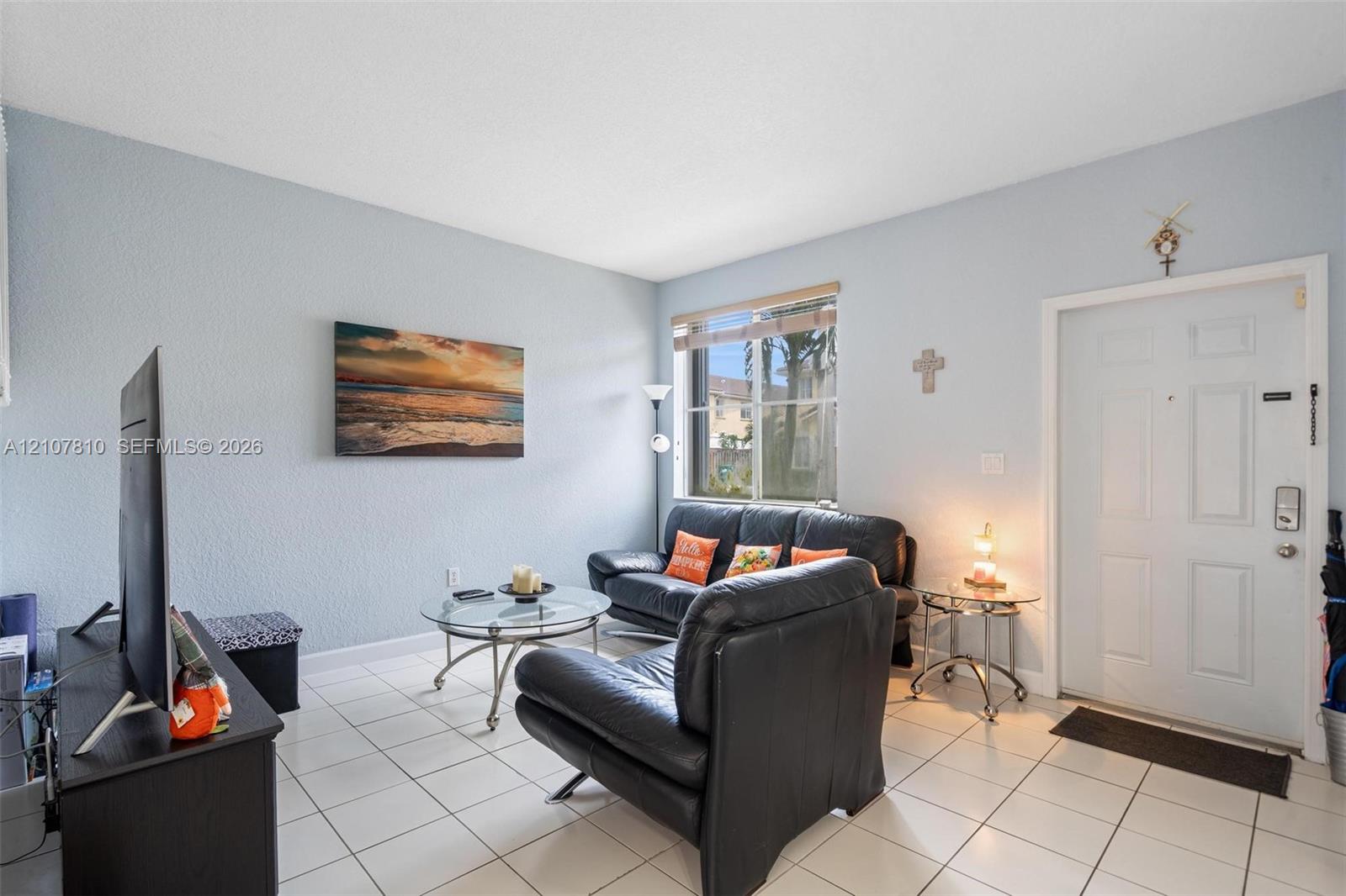 Living area featuring white ceramic tile flooring, neutral wall tones, and a window with horizontal blinds