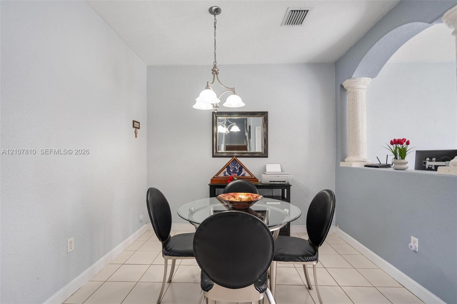 Interior area featuring ceramic tile flooring, a multi-light pendant chandelier, an arched wall cutout, and a decorative column