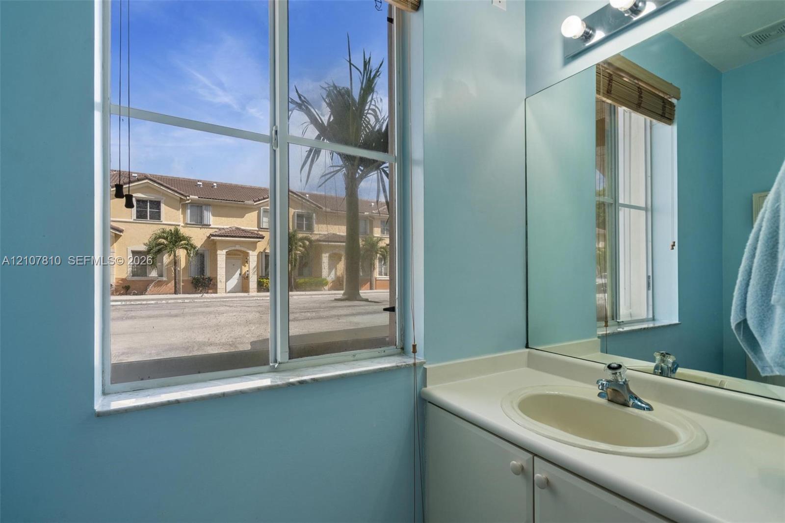 Bathroom vanity featuring an integrated countertop and sink, large wall-mounted mirror, multi-bulb overhead lighting, and a window with exterior exposure