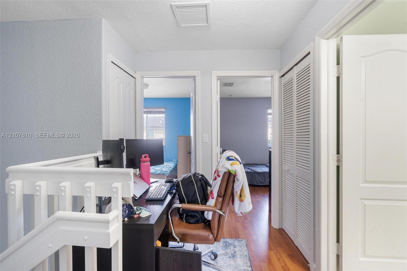Landing area featuring wood-finish flooring, a white wooden balustrade, and closet spaces with louvered bi-fold doors