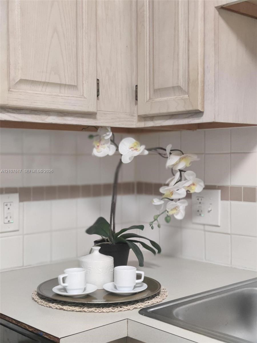 Light-tone wood cabinetry featuring recessed-panel doors, neutral solid-surface countertops, and square ceramic tile backsplash with decorative accent inlay