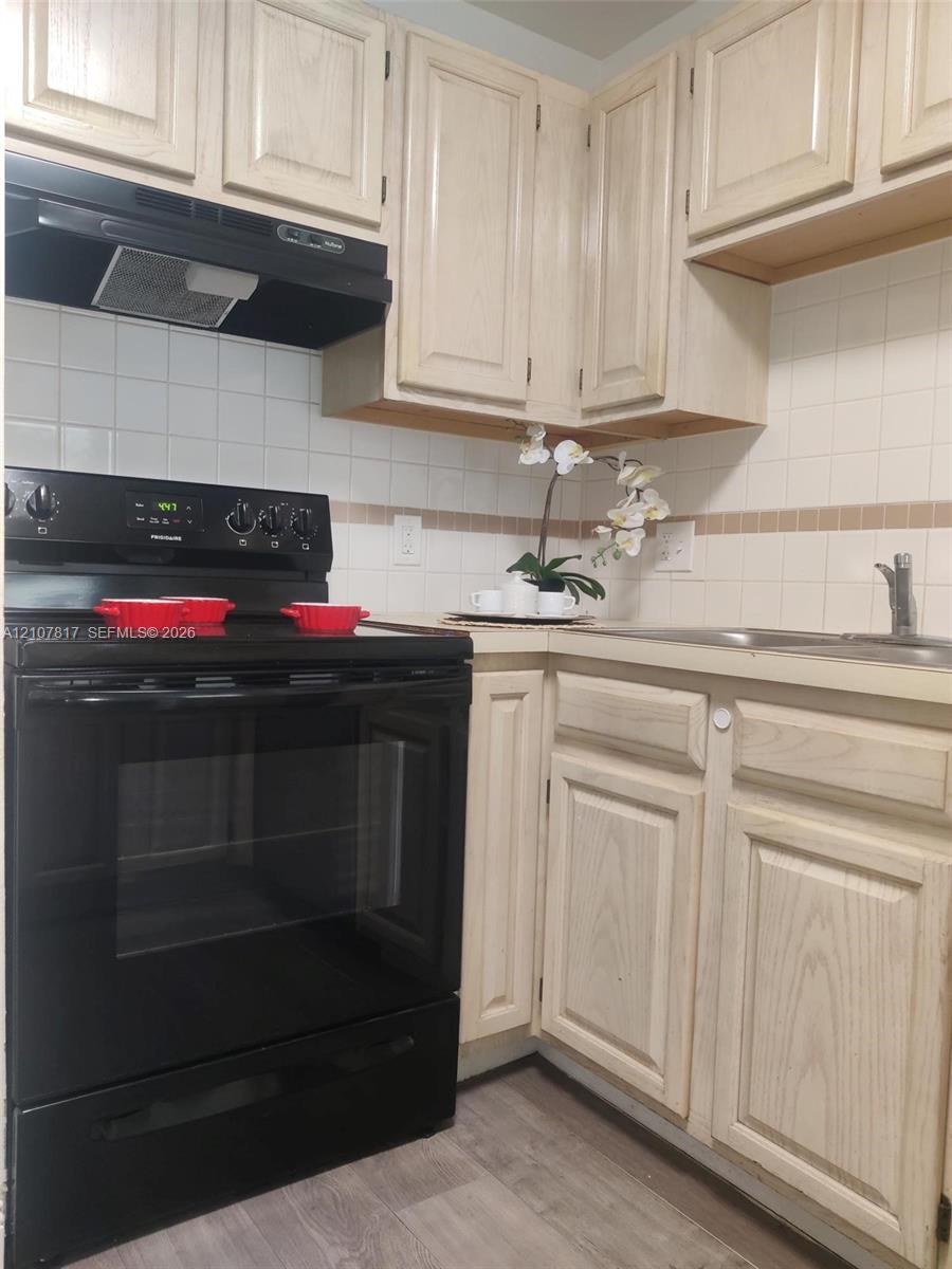 Kitchen featuring light-finish cabinetry, black freestanding range, matching black range hood, tiled backsplash, and wood-finish flooring