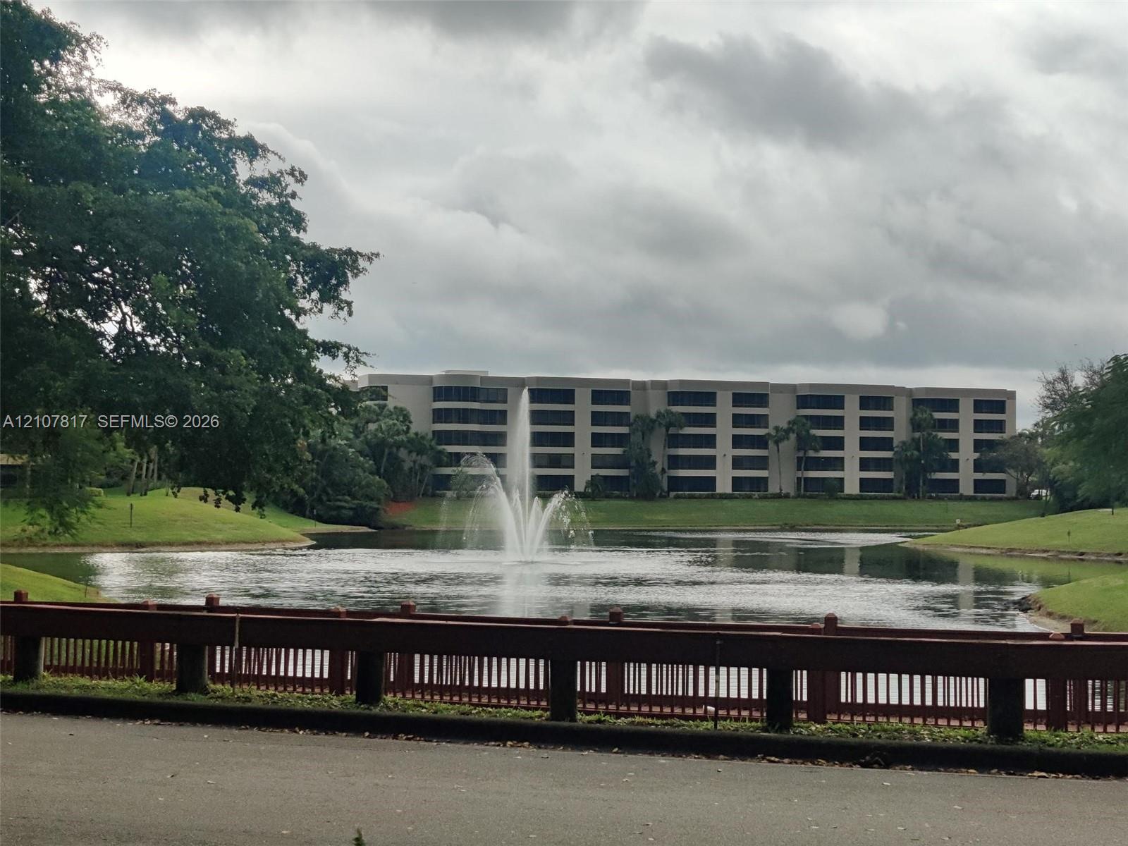 Multi-story building exterior featuring a central water fountain, landscaped grass slopes, and a perimeter railing
