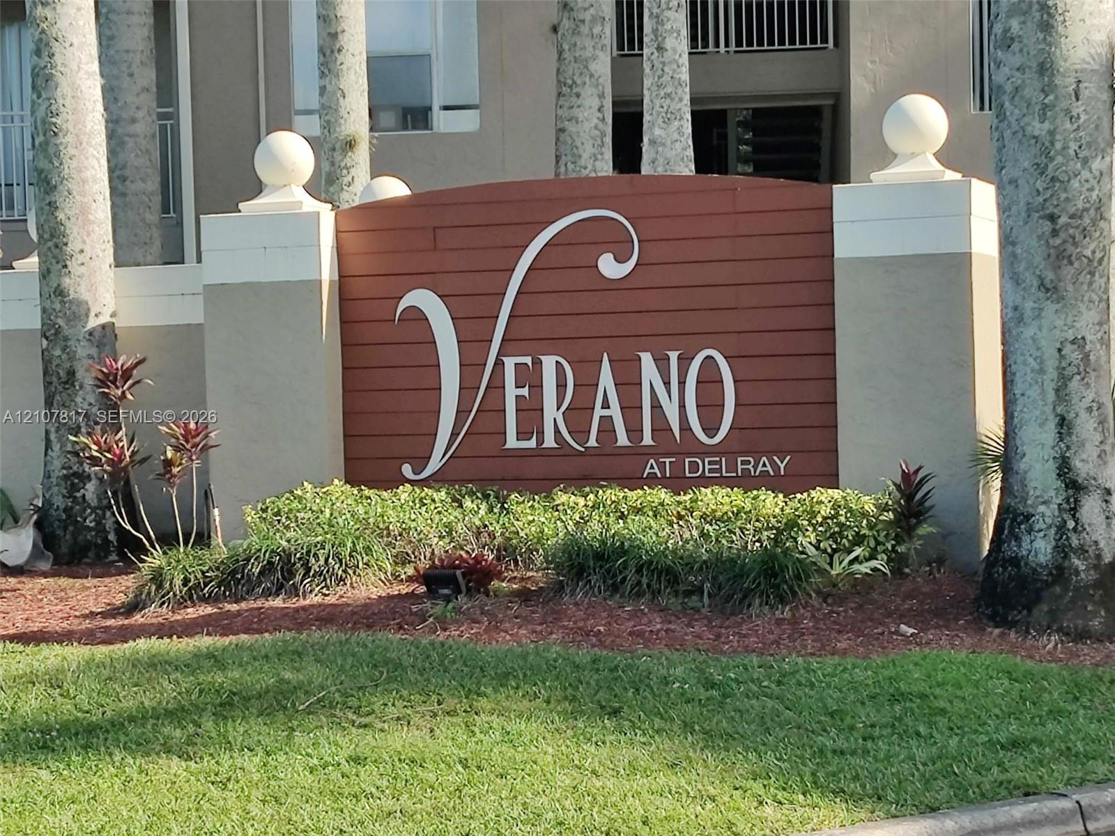 Community monument sign featuring horizontal wood-slat siding, decorative concrete pillars with ball finials, and professional landscaping