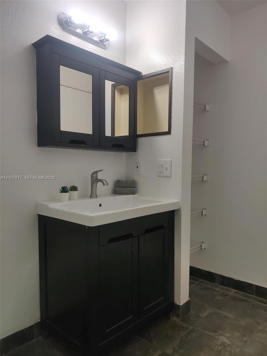 Dark wood-finish vanity with an integrated basin, wall-mounted mirrored medicine cabinet, single-handle brushed metal faucet, and built-in wire shelving