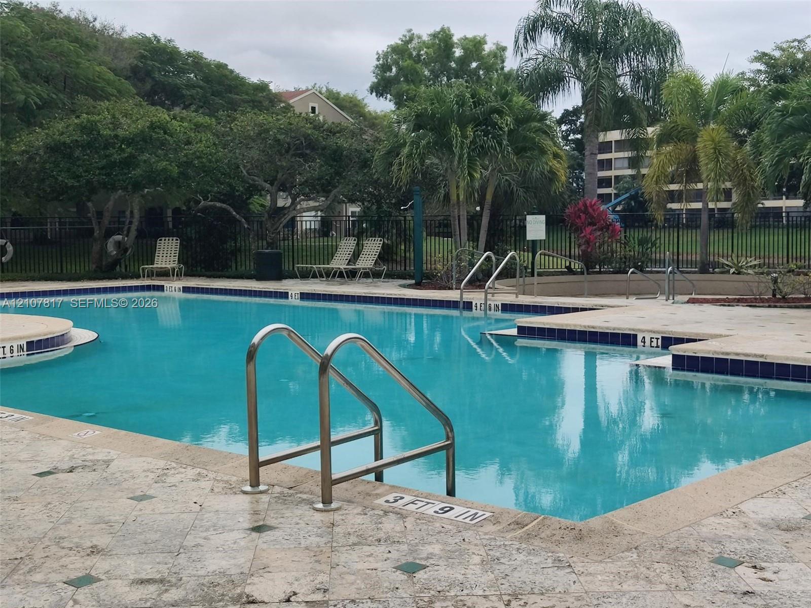 Swimming pool featuring tile trim, stone paver decking, integrated handrails, and mature landscaping