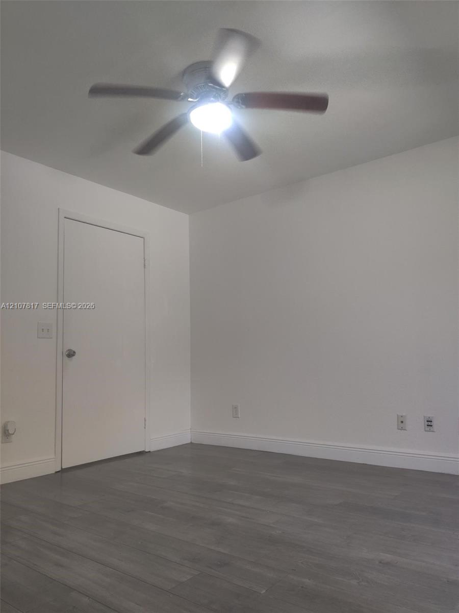 Room featuring wood-finish flooring, a neutral color palette, and a central ceiling fan with integrated lighting