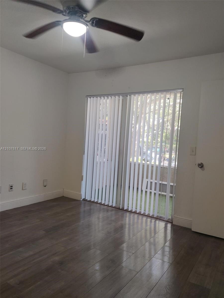 Interior space featuring wood-finish flooring, a ceiling fan with integrated light fixture, and vertical window blinds covering a sliding glass door