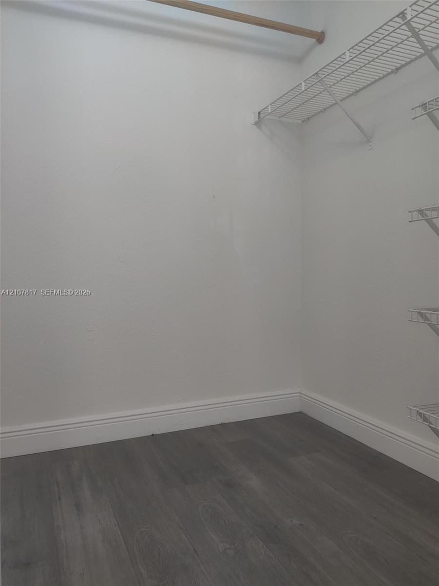 Storage area featuring wood-finish flooring and white shelving with an integrated hanging rod