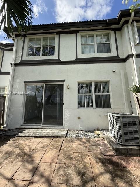 Exterior rear elevation featuring a stucco facade with dark trim, dual-pane multi-light windows, sliding glass door, and a paver patio Exterior rear elevation featuring a stucco facade with dark trim, dual-pane multi-light windows, sliding glass door, and a paver patio