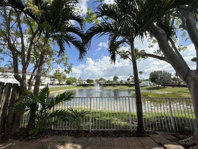 Outdoor brick patio featuring a metal fence enclosure, mature palm trees, and a pond with a central fountain Outdoor brick patio featuring a metal fence enclosure, mature palm trees, and a pond with a central fountain
