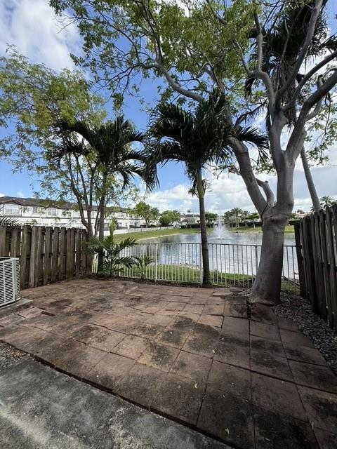 Rear patio featuring stone pavers, enclosed by wood fencing and a metal railing, complemented by mature trees and a fountain Rear patio featuring stone pavers, enclosed by wood fencing and a metal railing, complemented by mature trees and a fountain