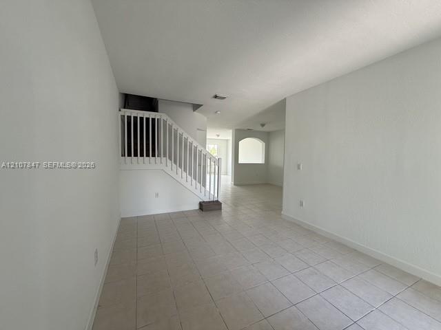 Open-concept interior featuring neutral tile flooring, white walls, a staircase with a white railing, and a decorative archway Open-concept interior featuring neutral tile flooring, white walls, a staircase with a white railing, and a decorative archway
