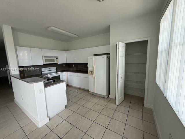 Kitchen featuring white cabinetry, dark countertops, tiled flooring, an integrated pantry, and a peninsula Kitchen featuring white cabinetry, dark countertops, tiled flooring, an integrated pantry, and a peninsula