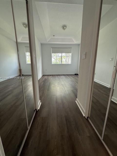 Room featuring wood-finish flooring, a tray ceiling, dual mirrored sliding closet doors, and a window with a roller shade