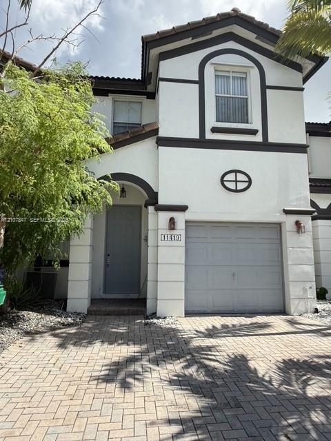 Two-story exterior featuring a stucco facade, arched entryway, brick-patterned paver driveway, single-car garage, and decorative oval window detailing Two-story exterior featuring a stucco facade, arched entryway, brick-patterned paver driveway, single-car garage, and decorative oval window detailing