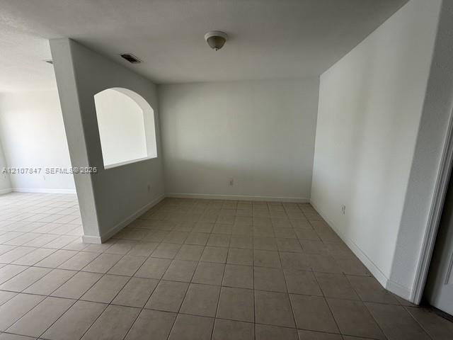 Interior space featuring neutral tile flooring, smooth white walls, a structural arched wall cutout, and a ceiling-mounted light fixture Interior space featuring neutral tile flooring, smooth white walls, a structural arched wall cutout, and a ceiling-mounted light fixture