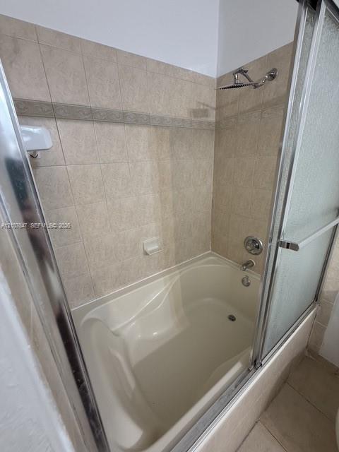 Bathtub and shower combination featuring neutral-toned tile wall surround, decorative accent tile border, chrome shower head, and sliding glass enclosure