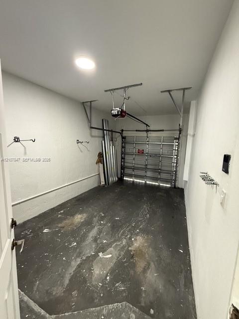 Enclosed garage featuring an automated overhead door system, ceiling-mounted lighting, and wall-mounted storage hardware Enclosed garage featuring an automated overhead door system, ceiling-mounted lighting, and wall-mounted storage hardware
