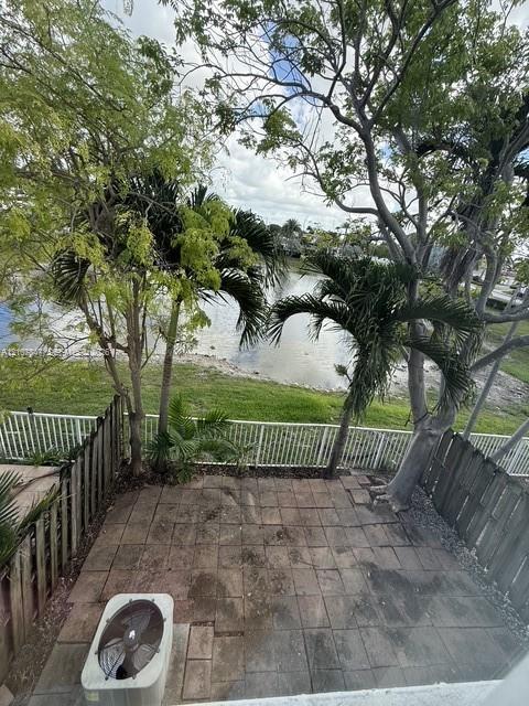Paved patio featuring a water-front location, perimeter wood fencing, and mature trees