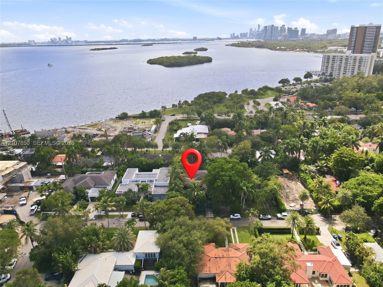 Aerial perspective of a coastal residential lot featuring mature tree canopy, significant landscaping, and proximity to the waterfront