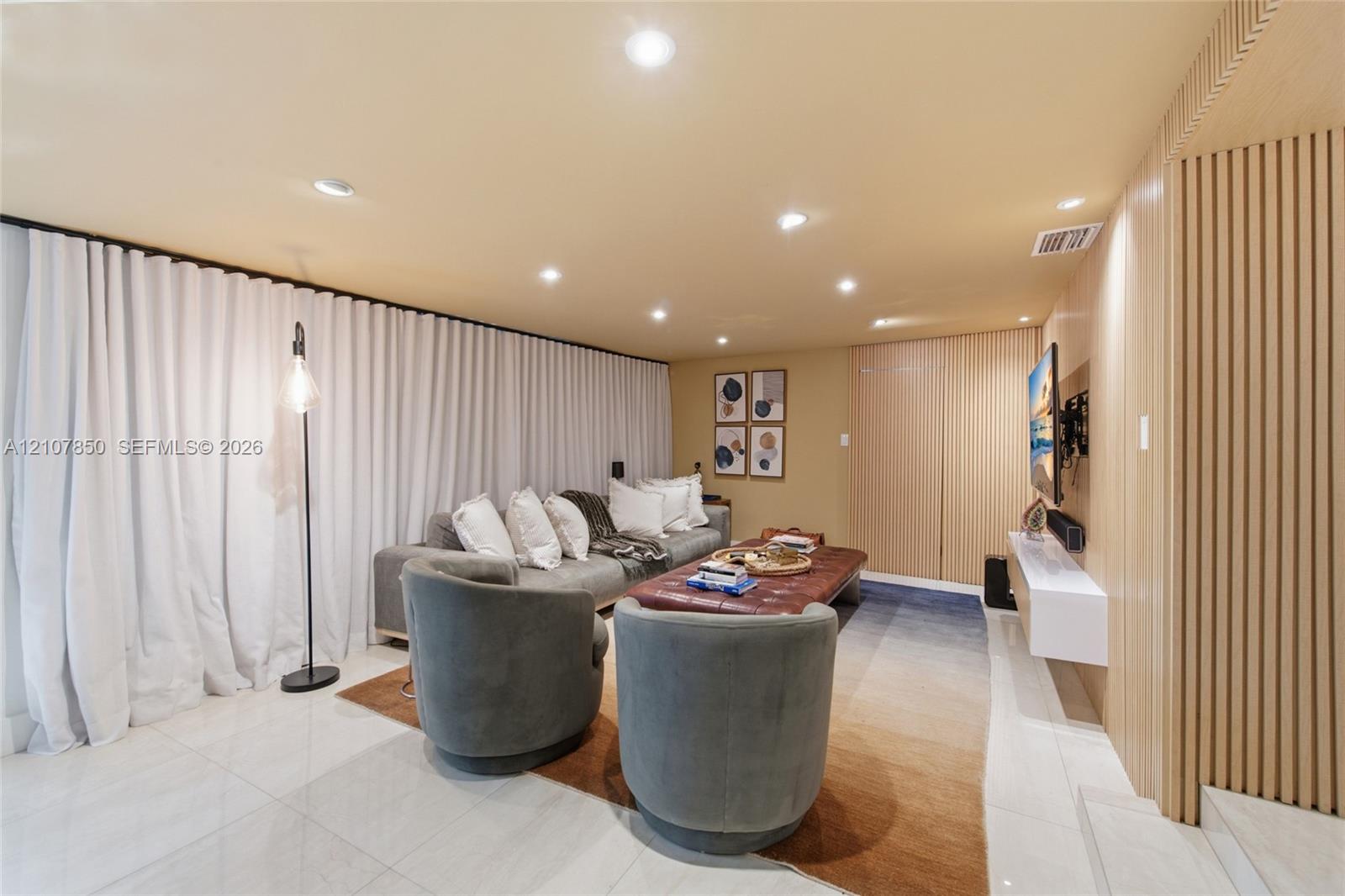 Interior space featuring large-format tile flooring, recessed ceiling lighting, a wall-mounted floating media console, and vertical wood-slat wall paneling