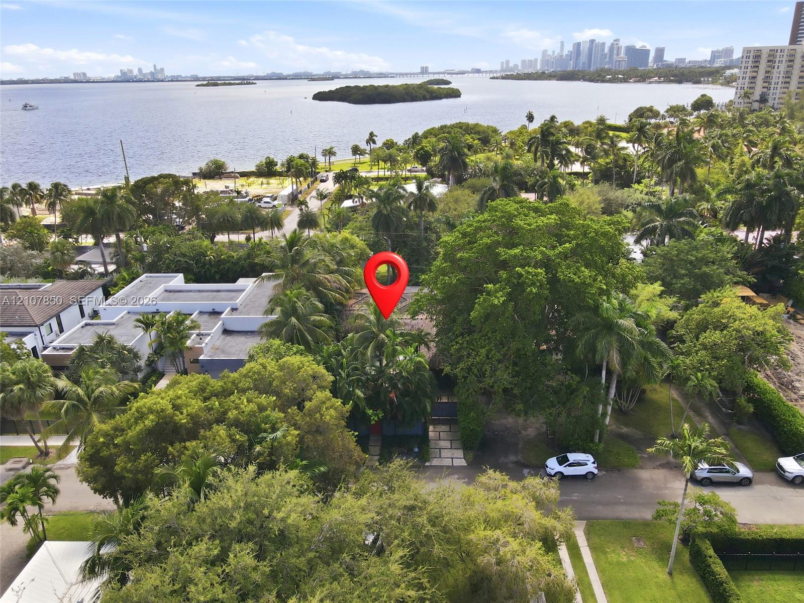 Aerial perspective of a property featuring mature tropical landscaping, a multi-car driveway with paved hardscaping, and proximity to the waterfront