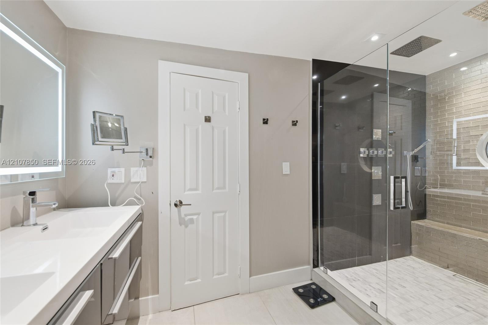 Bathroom featuring a dual-sink vanity with light-toned countertop, walk-in shower with glass enclosure, integrated bench seating, and recessed ceiling lighting
