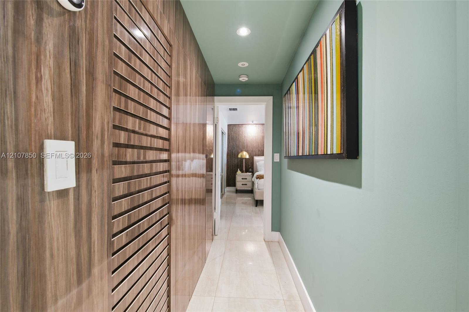 Hallway featuring polished tile flooring, vertical wood-panel wall treatments, louvered built-in cabinet doors, and recessed ceiling lighting