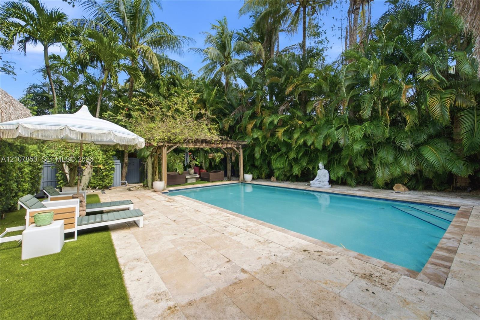 In-ground swimming pool with stone coping, natural stone pool deck, wooden pergola, and established tropical vegetation